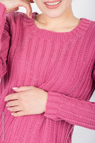 Beauty, fashion and style concept. Woman torso with purple sweater. Beautiful model body shape. Studio shot with copy space. Hand placed on belly with pink manicure
