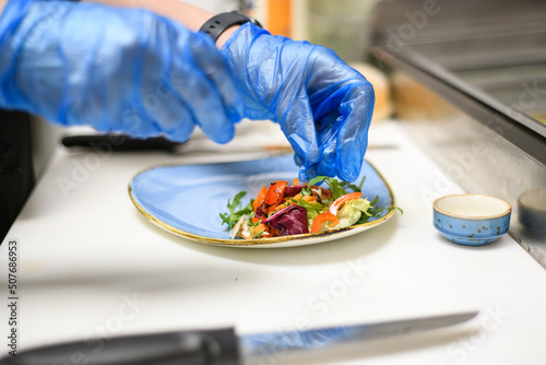 Close-Up of a person wearing disposable protective gloves putting salad on a plate in a cafe
