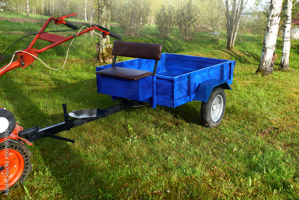 Fototapeta premium A new cargo trailer for a walk-behind tractor against the backdrop of a rural landscape. Preparing for the summer season.