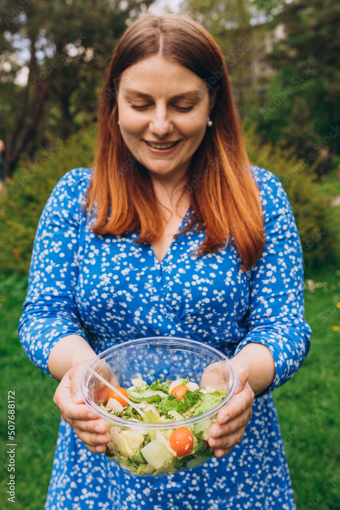 Hands of happy redhead woman holding bowl with salad over isolated nature background. Healthy picnic, food banner Hands of happy redhead woman holding bowl with salad over isolated nature background. Healthy picnic, food banner