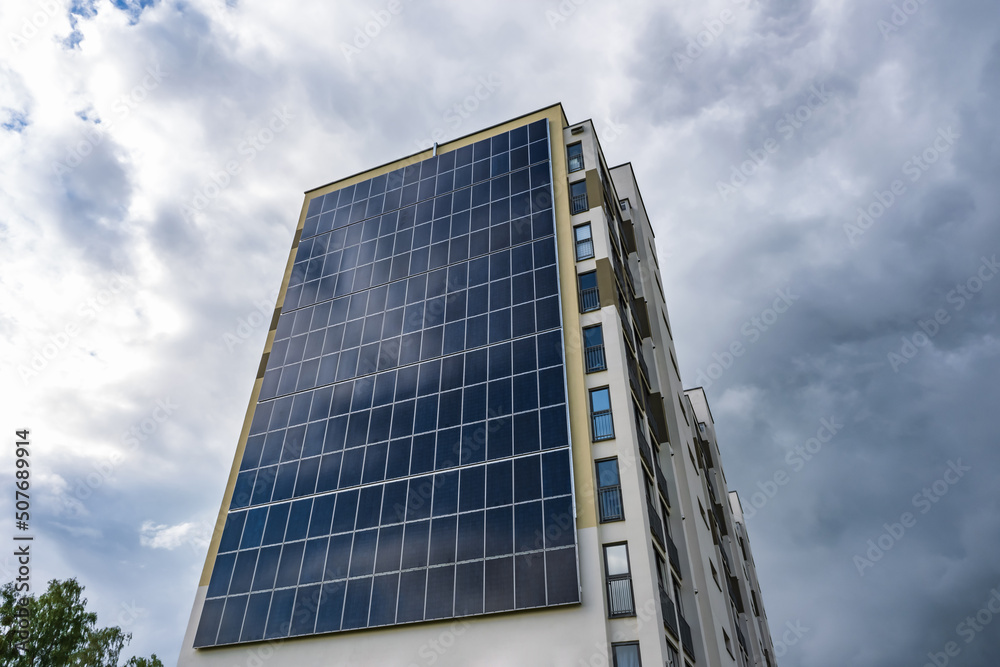 Fototapeta premium solar panels on the wall of a multi-storey building on storm clouds background. Renewable solar energy. an energy-efficient home that uses the energy of the earth, sun, air and wastewater