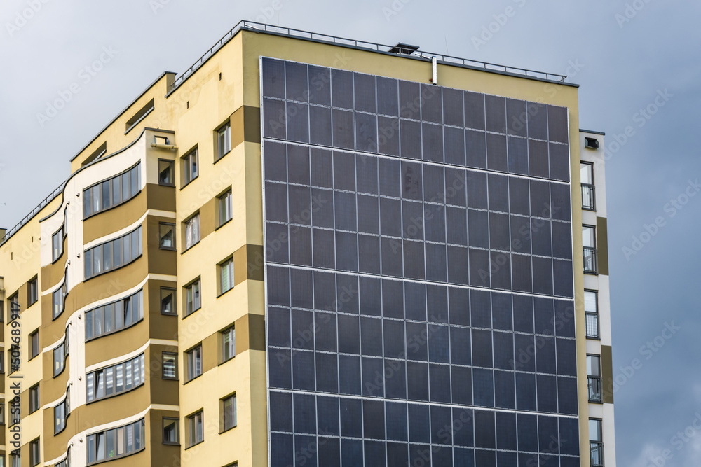 Fototapeta premium solar panels on the wall of a multi-storey building on storm clouds background. Renewable solar energy. an energy-efficient home that uses the energy of the earth, sun, air and wastewater