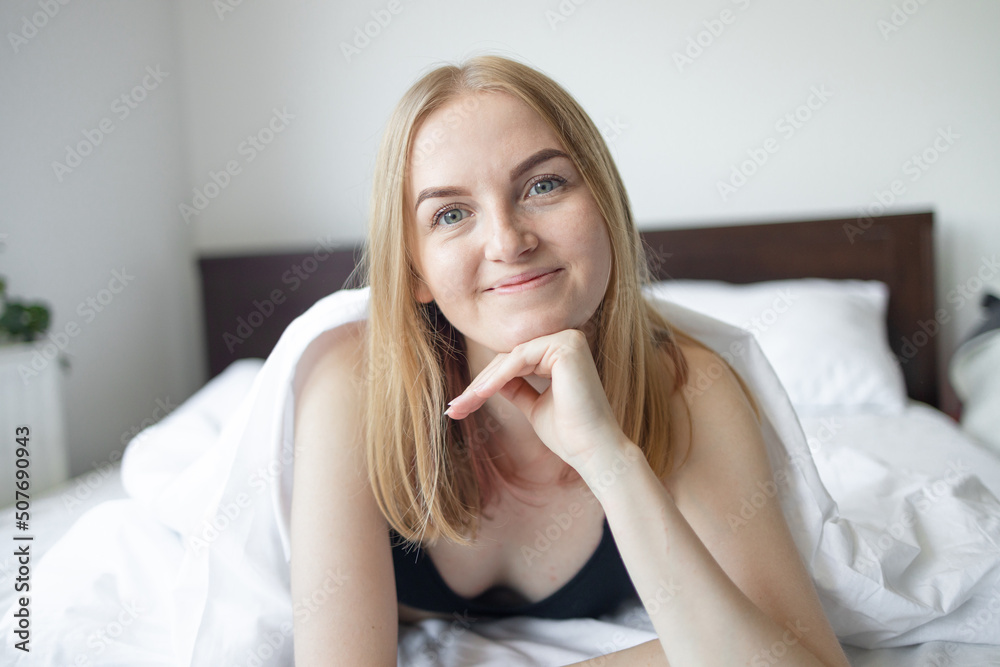 Young beautiful girl smiling after wake up in her bed with white bedclothes early in the morning. Young beautiful girl smiling after wake up in her bed with white bedclothes early in the morning.