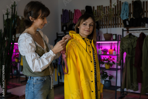 Making measures before tailoring. Fashion designer workshop with female tailor measuring and fitting bespoke rain jacket. Young woman small dressmaking business owner at workplace. Needlework concept 