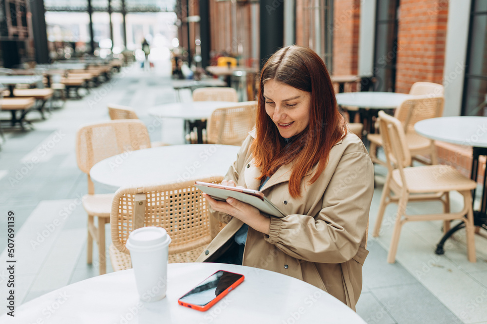 Young woman enjoying a coffee, sitting on the cafe terrace on the modern city street. Person sitting at table and using tablet outdoors. Traveler, Online education, working or shopping concept Young woman enjoying a coffee, sitting on the cafe terrace on the modern city street. Person sitting at table and using tablet outdoors. Traveler, Online education, working or shopping concept