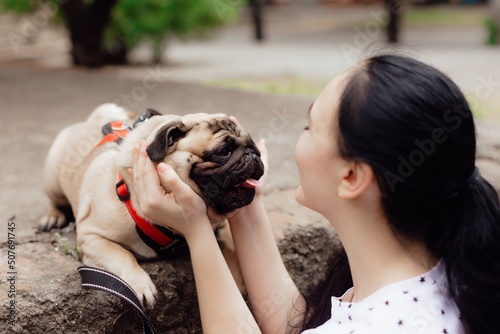 Young girl goes for walk with doggy pug in park. Selective focus.