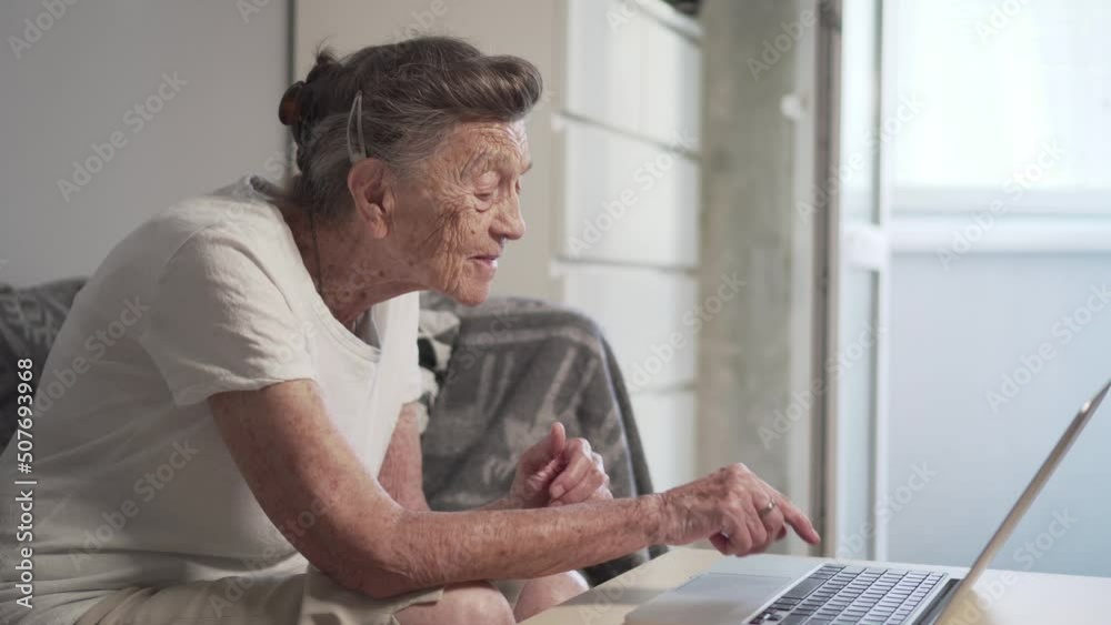 Elderly woman having a video call with family, smiling and waving. Senior woman with gray hair make video call using laptop at home. COVID-19 Stay connected. Online chatting with long distance friends Elderly woman having a video call with family, smiling and waving. Senior woman with gray hair make video call using laptop at home. COVID-19 Stay connected. Online chatting with long distance friends