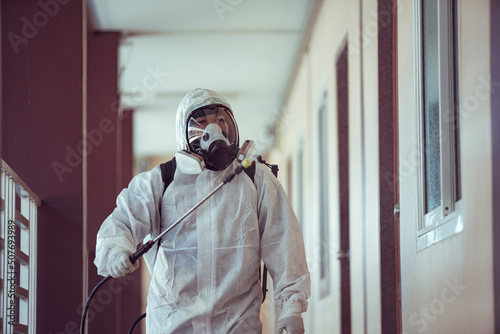 Cleaner in PPE spraying disinfectant inside a building photo