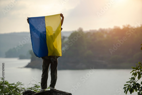 Rear view of a woman standing by a river holding a Ukrainian flag above her head, Thailand photo