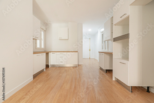 Photo of a newly installed kitchen awaiting appliances  open to a living room with white wood cabinets with wood countertops and matching wood flooring.