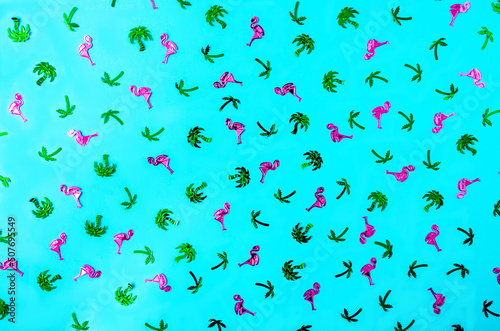 A shiny pattern made of pink flamingos and green palm trees against blue background. Seamless wallpaper or background for summer season banner or advertisement. Flat lay.