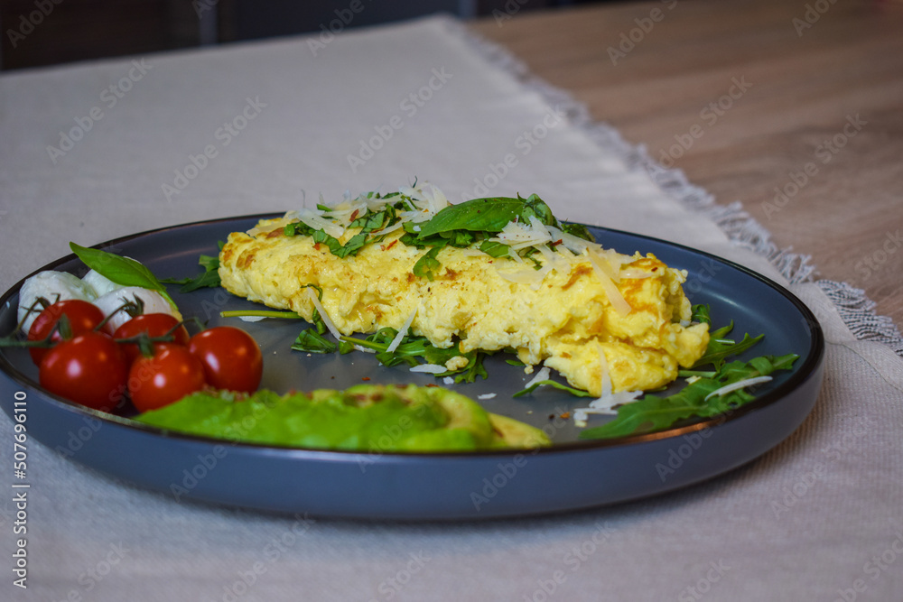 French omelette dish. Delicous homemade french omlette filled with cheese. Plating with fresh vegetables like avocado, cherry tomatoes, but also basil and mozzarella.