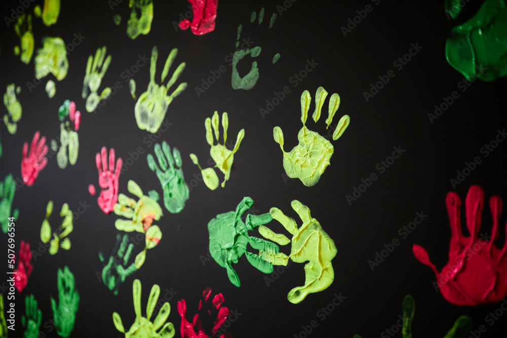 multicolored handprints on a black background. Handprints in acrylic