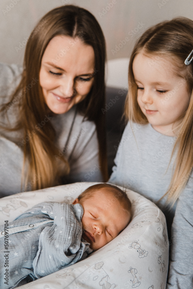 Close-up portrait of mother with newborn son and infant daughter. Happy caucasian family of three people. Sister meets her newborn brother. Selective focus. Film grain