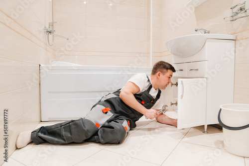 A male plumber repairs siphon under the sink in the bathroom.