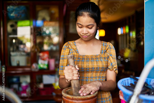 teenage thai girl using mortar and pestle in kitchen