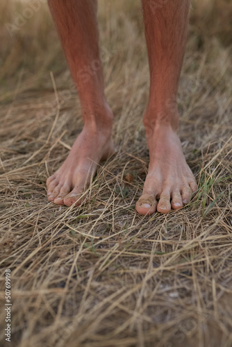 The guy stands on dry grass barefoot. Legs close up. 