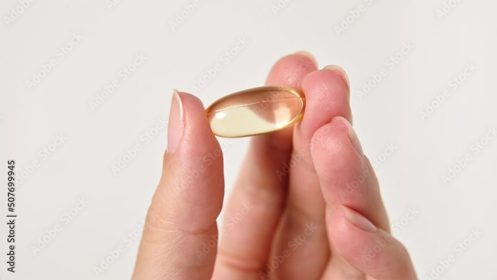Hand of young woman, girl holds golden capsule with Omega 3 on light background. Vitamins, pills, vitamin d, Supplements, pharmaceutical theme, healthy lifestyle, medicine. Fish oil pill Hand of young woman, girl holds golden capsule with Omega 3 on light background. Vitamins, pills, vitamin d, Supplements, pharmaceutical theme, healthy lifestyle, medicine. Fish oil pill