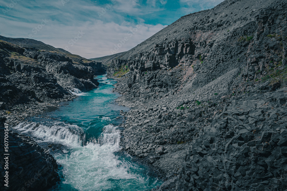 Aerial drone panorama of studlagil canyon in Iceland, picturesque valley with basalt columns standing high on a warm summer day. Closeup of the basalt tiwers in the water