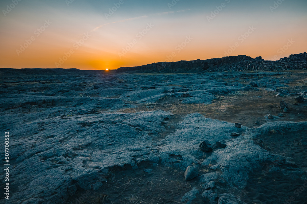 Magnificent rock formations in the Dettifoss area in Iceland during summer sunset, blue rock surrounded by beautiful orange light on the sky with flare from setting sun.