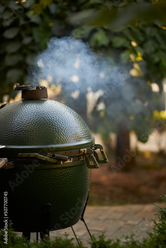 portable grill in the yard. Side view of a portable barbecue grill with a lid in front of the house or in the backyard and a green lawn. photo