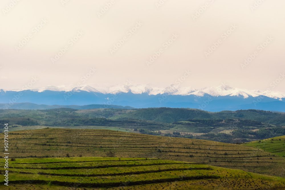 Beautiful landscape view a panoramic view of the Retezat mountains, Carpathians, Romania. View of the snowy peaks behind the colorful fields.