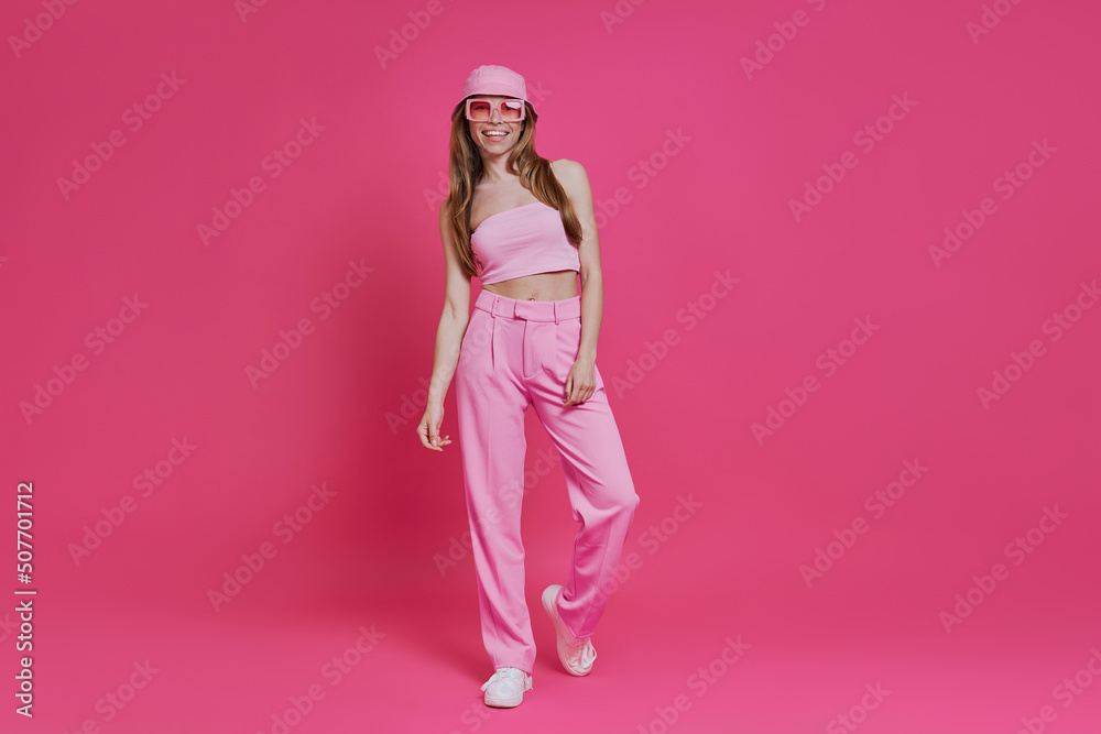 Full length of beautiful young woman in trendy clothing standing against pink background