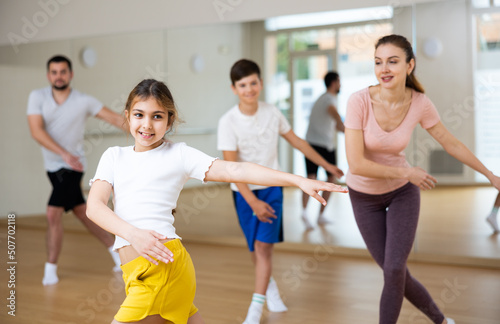 Cheerful girl exercising in family group during dance class at dance studio