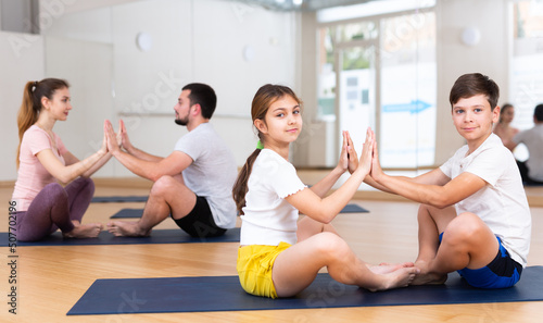 Teen girl and boy exercising with mother and father at couple yoga class, family practicing self-care