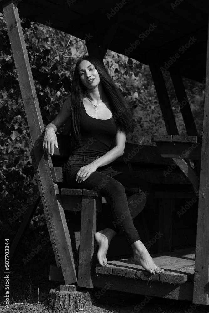 Beautiful slender barefoot woman in wooden gazebo in black and white