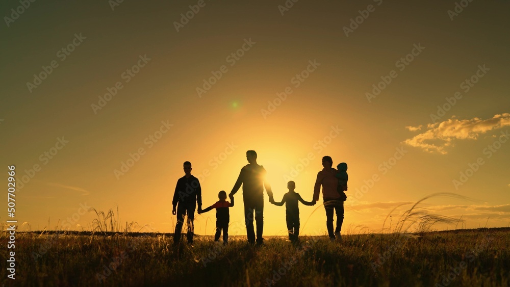 Happy big family with children are walking in park, sun. People travel in nature. Mom, dad, son are walking together on grass, holding hands, teamwork. Family walk on field. Healthy big family concept