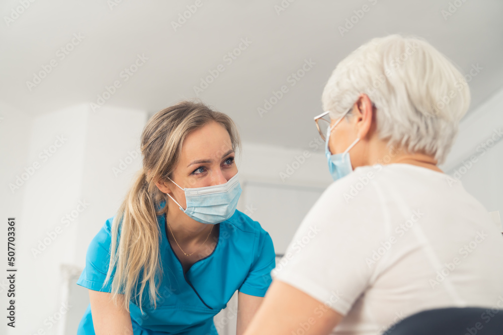 Young caucasian female nurse helping and looking at an elderly woman, both are wearing masks. Helthcare concept. Inner shot. High quality photo