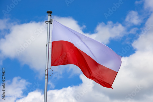 Polska flaga biało-czerwona powiewająca na maszcie na tle błękitnego nieba photo