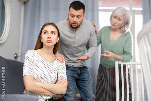 Depressed young woman ignoring her husband and mother quarreling with her in apartment. © JackF