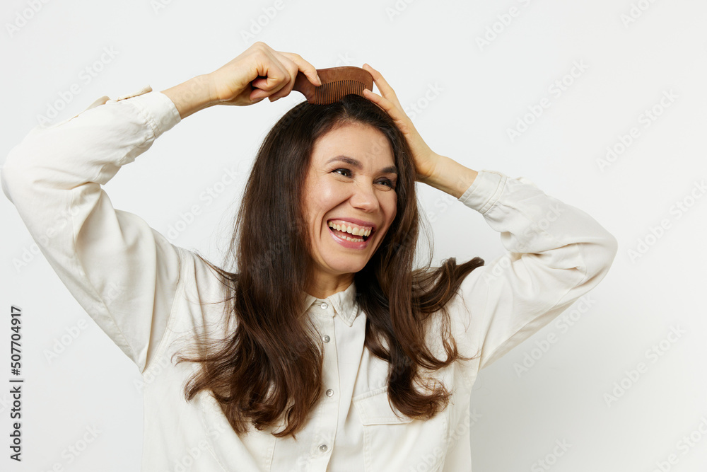 joyful happy woman combing her hair with a wooden comb smiling joyfully. Horizontal photo on a light background joyful happy woman combing her hair with a wooden comb smiling joyfully. Horizontal photo on a light background