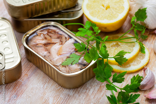 Closeup view of opened can of preserved chopped tuna belly in olive oil on wooden surface with ingredients for cooking