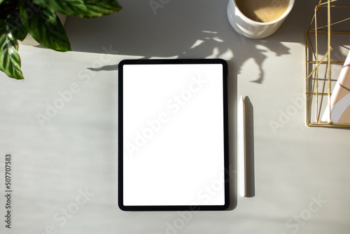 Digital tablet with blank screen mockup, pen, cup of coffee, plant on home office desk table. Freelancer workspace top view. photo