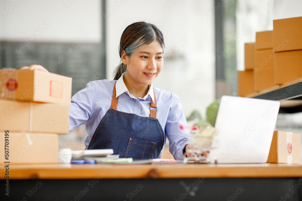 Young Asian entrepreneur SME woman checking product on stock take note with a laptop. Small business owner working at home. Check address on the parcel SME online start up freelance concept. Young Asian entrepreneur SME woman checking product on stock take note with a laptop. Small business owner working at home. Check address on the parcel SME online start up freelance concept.