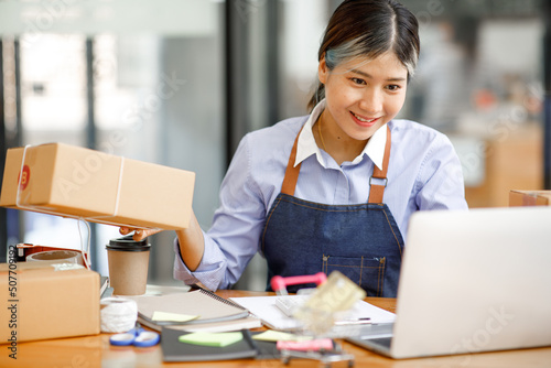 Young Asian entrepreneur SME woman checking product on stock take note with a laptop. Small business owner working at home. Check address on the parcel SME online start up freelance concept.