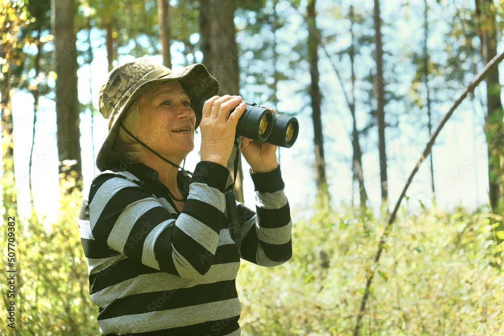 Active smiling senior woman with binoculars in the forest. Traveling, hiking, walking, enjoying vacations Active smiling senior woman with binoculars in the forest. Traveling, hiking, walking, enjoying vacations