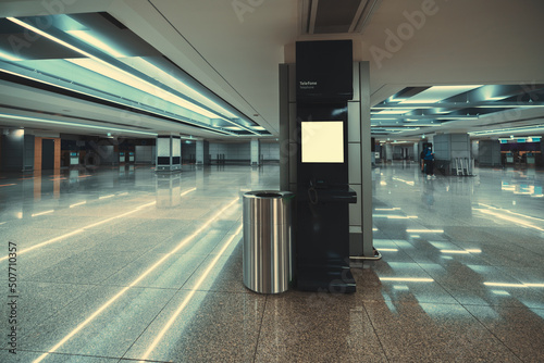 A wide-angle view of a modern opened phone booth with a payphone indoors of a contemporary airport terminal or a waiting hall of a railway station depot with plenty of reflections on the marble floor