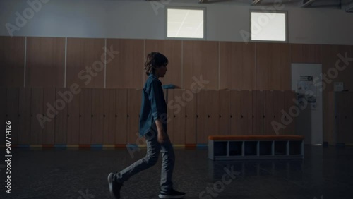 Relaxed pupil walking dark school hall alone. Teen schoolboy passing lockers. photo