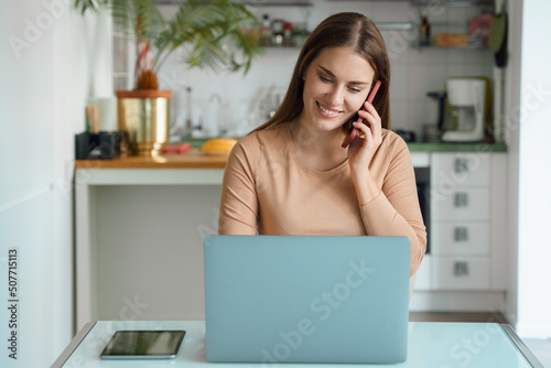 Young woman freelancer talking phone while working online on laptop