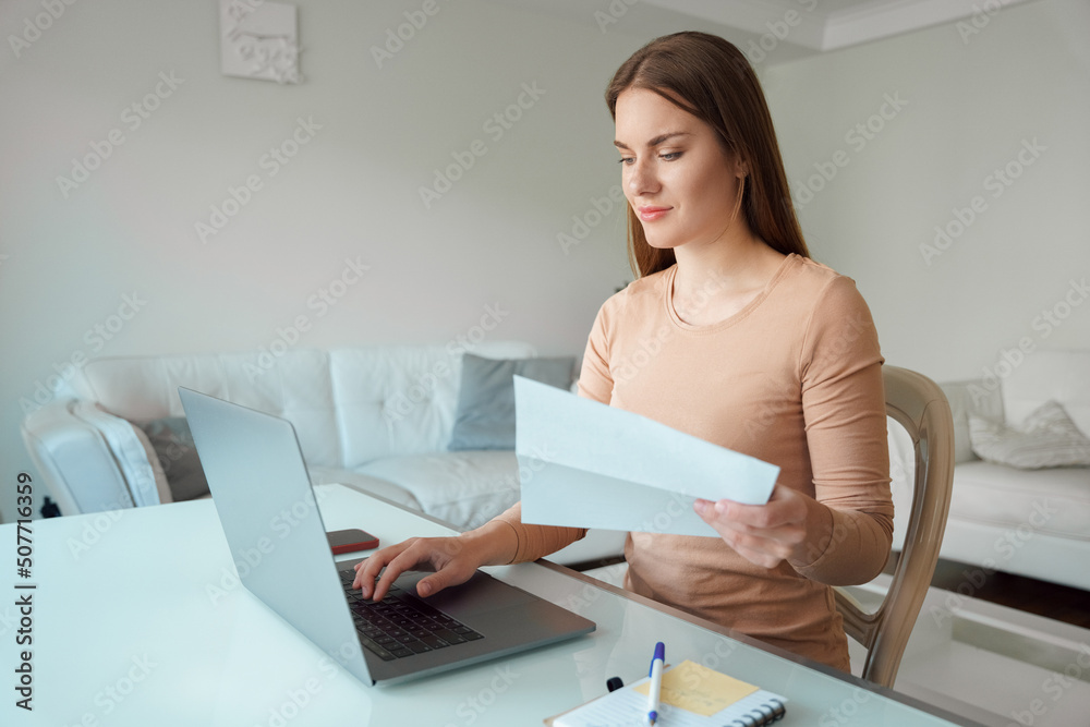 Obraz premium Young woman holding paper document sitting front of laptop