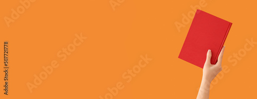 Hand holding book on orange background with space for text