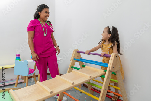 girl climbing a game in the pediatric office, while the pediatrician observes her photo