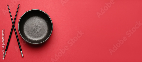 Chinese bowl with chopsticks on red background with space for text