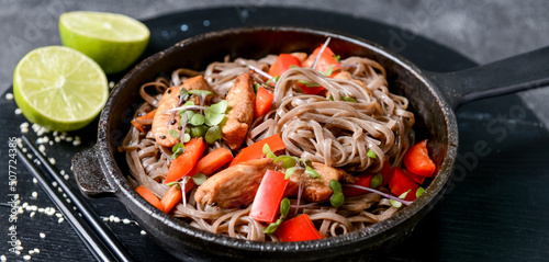 Frying pan with tasty soba noodles and meat on dark background, closeup