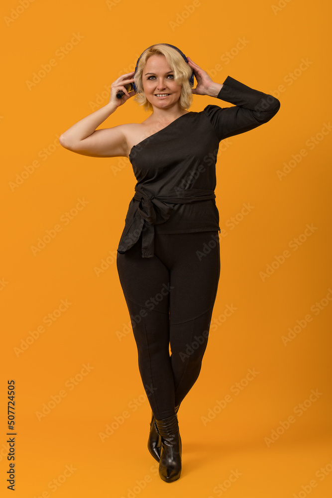 blonde woman in black clothes with a bare shoulder in headphones on a colored background blonde woman in black clothes with a bare shoulder in headphones on a colored background