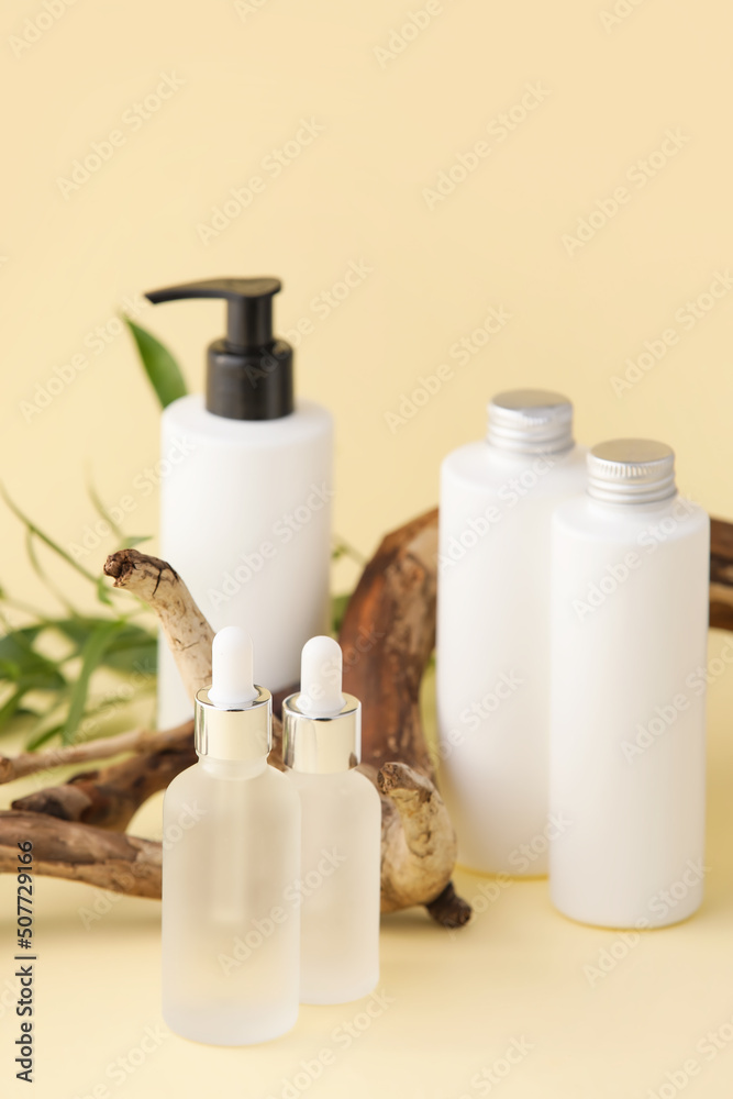 Bottles of natural serum, tree branch and plant leaves on yellow background Bottles of natural serum, tree branch and plant leaves on yellow background